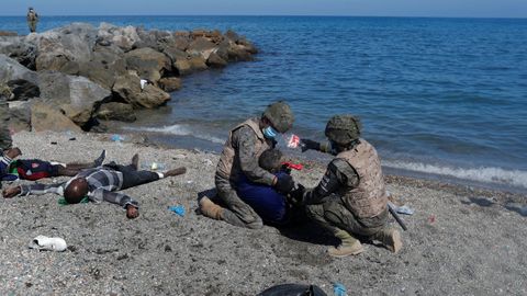 Dos soldados ayudan a uno de los inmigrantes que han llegado a la playa de El Tarajal