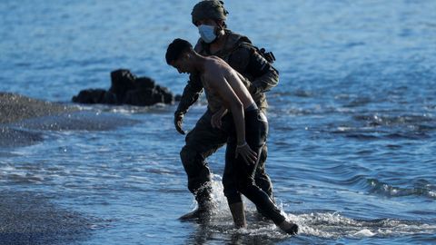 Un militar ayuda a un joven marroquí a su llegada a la playa