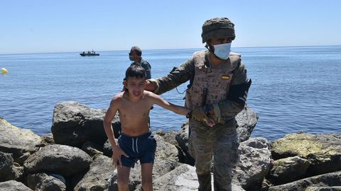 Un militar español ayuda a un menor migrante a salir del agua en la playa del Tarajal