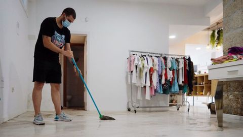 Guillermo Blanco, de la tienda de ropa Xeitos, limpiando el local tras las inundaciones