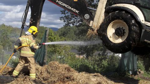 Un bombero remoja el tractor que los ayudaba a sacar la hierba, que casi empieza a arder por debajo