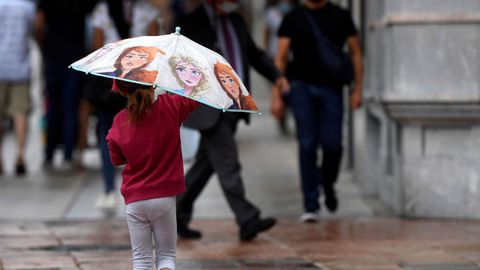 Una niña se protege esta tarde de la lluvia en una céntrica calle de Oviedo