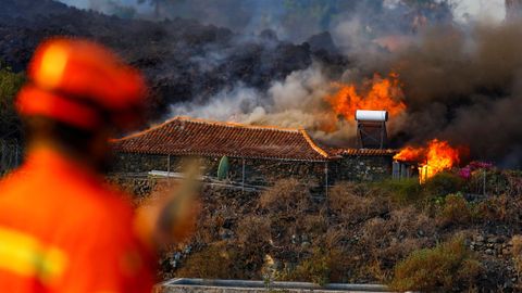 Un miembro de Protección Civil observa un casa que arde por el efecto de la lava