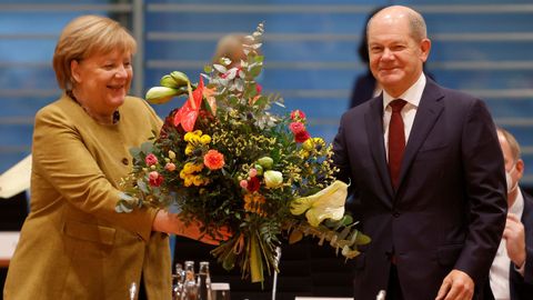 Angela Merkel recibe un ramo de flores de su sucesor Olaf Scholz durante la última reunión de su gabinete en Berlín.