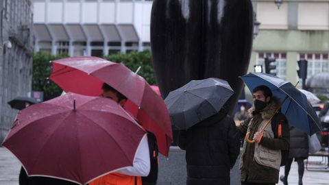 Unos turistas se protegen de la lluvia junto a una estatua de rculo, en Oviedo