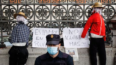 Un agente de Policía Nacional frente a dos espantapájaros colocados junto a dos carteles en los que se leen: «Estamos en la ruina, no aguantamos más» colocados durante una manifestación de agricultores en Madrid el pasado 24 de noviembre