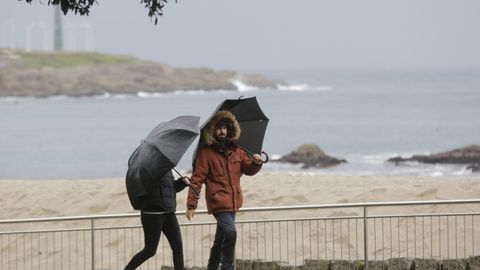 Obligatorio llevar paraguas hoy en la comunidad gallega. En la imagen, gente paseando por el paseo marítimo de A Coruña
