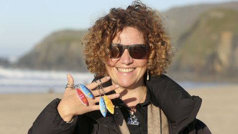 Iria García muestra parte de la colección de llaveros inspirados en el surf, con la playa al fondo