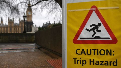 Una seal de advertencia por riesgo de tropiezo, sobre la imagen, al fondo, del Parlamento britnico