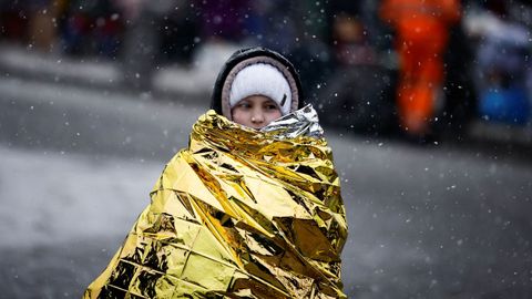 Una persona que huye de la invasión rusa de Ucrania se sienta durante una nevada mientras llega a un campamento temporal en Przemysl, Polonia