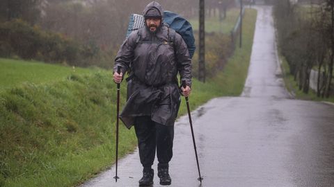 Un peregrino camina bajo la lluvia con pantalón impermeable, chubasquero y una funda para la mochila.