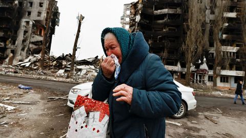 Nina, de 74 años, llora mientras camina al lado de un edificio destruido por las bombas rusas.