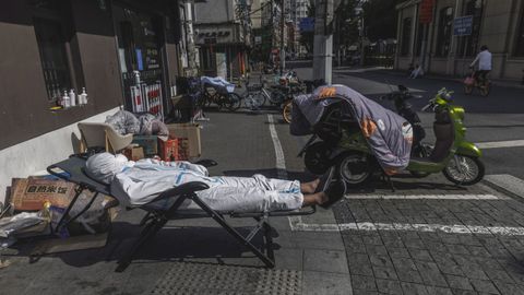 Un repartidor duerme la siesta en una calle de Shanghi sin quitarse el traje de proteccin contra el covid