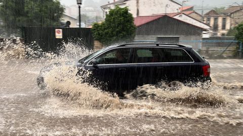 Un coche circula por una calle de Oviedo que se encuentra inundada tras las últimas lluvias registradas en la región.