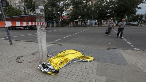 Dos peatones observan el cadáver cubierto de una de las víctimas del ataque con bombas racimo en Mykolaiv
