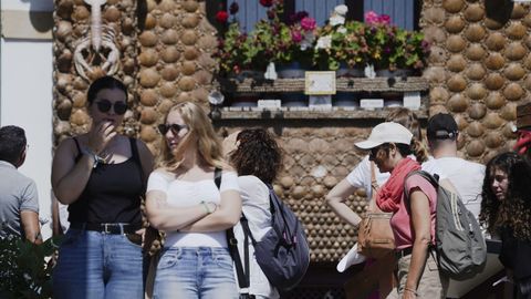Turistas pasan ante una casa decorada con conchas en Tazones, Asturias