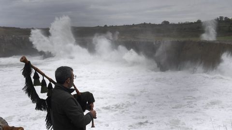 Un hombre toca su gaita mientras las olas gigantes rompen en los Bufones de Pría