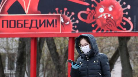 Una mujer camina con una mascarilla y guantes frente a una pancarta que representa el coronavirus y en el que pone  Ganaremos , en Minsk, Bielorrusia