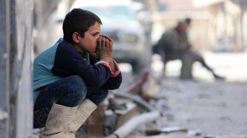 Un nio sirio, sentado en la acera de una calle de la ciudad de Ghouta 