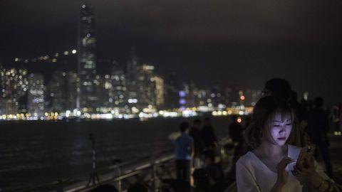 Una mujer observa su mvil de espaldas al skyline de Hong Kong, durante el apagado de luces