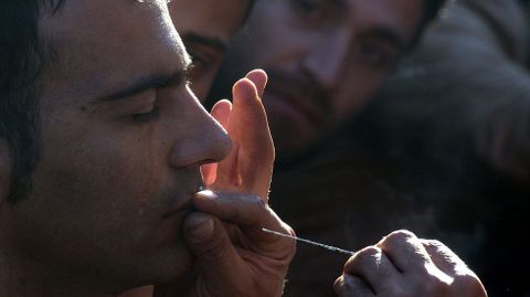 Un emigrante cose los labios de un camarada iran como acto de protesta contra las restricciones impuestas por los pases balcnicos para el paso de migrantes.