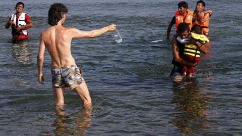 Un turista ofrece agua a unos inmigrantes irans que llegan a la Isla de Kos