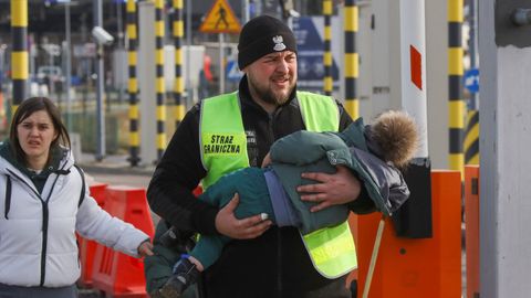 Un miembro de la guardia fronteriza polaca sostiene a un niño en un paso fronterizo entre Polonia y Ucrania, mientras los guardias fronterizos polacos cierran los carriles para vehículos para permitir un mayor tráfico de peatones. En Medyca, Polonia.