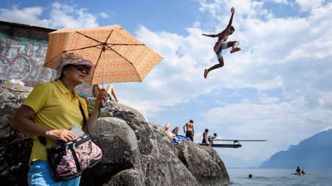 Un joven salta al agua del lago Geneva, en Saint Sahporin, en Suiza, mientras una turista se protege del sol