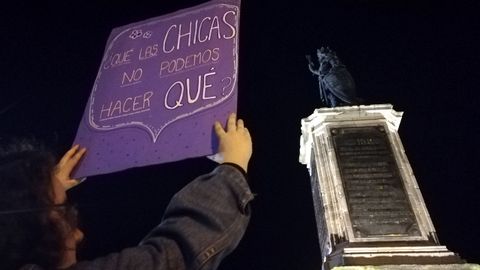 Una joven sostiene un cartel ante la estatua del rey Pelayo