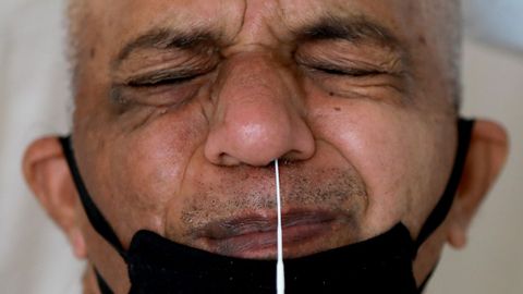 Un hombre que usa una mscara facial protectora reacciona cuando un mdico introduce un hisopo en su nariz para detectar la enfermedad del coronavirus, en India