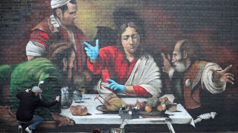 El artista Lionel Stanhope pinta un mural en Londres que representa la Cena de Emaús, de Caravaggio, con guantes protectores