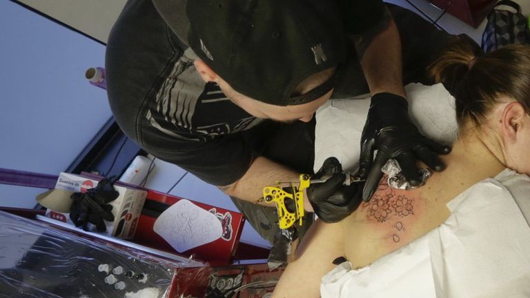 Imagen de archivo de un tatuador pigmentando en la espalda a una joven 