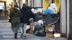 Dos personas caminan al lado de dos contenedores desbordados de basura en la calle Galera el 20 de diciembre