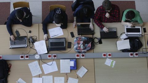 Alumnos con ordenadores y apuntes a mano en la facultad de Informática de Elviña