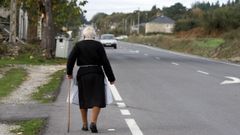 Una mujer jubilada pasea por el arcén de una carretera en Friol, Lugo
