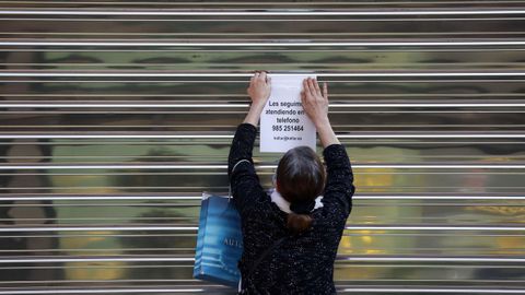 Una mujer coloca un aviso en la persiana cerrada de un negocio del centro de Oviedo, durante el estado de alarma