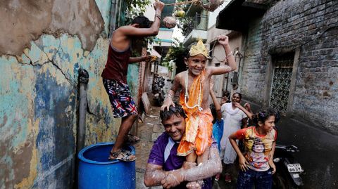 Un hombre lleva a su hijo vestido como Krishna en brazos.