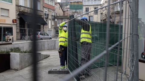 Dos obreros colocan una malla sobre las vallas instaladas a primera hora en la plaza Doutor Goyanes
