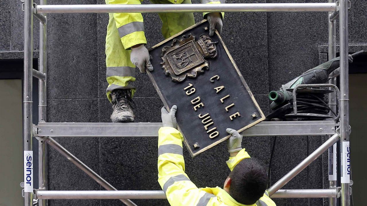 Dos operarios trabajan en la sustitución de la placa de la calle 19 de Julio, en el centro de Oviedo, en aplicación de la ley de Memoria Histórica por parte del Ayuntamiento de Oviedo