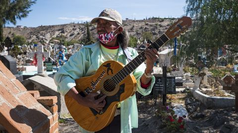 Un hombre con mascarilla toca la guitarra en un cementerio mexicano