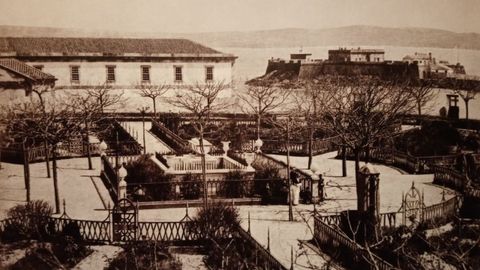 El jardín de San Carlos, en 1883, en la primera fotografía que se conoce, con el antiguo hospital y el castillo de San Antón al fondo. Los árboles son robinias. Aún no se habían plantado los olmos ni los setos que rodean los parterres actuales. El muro perimetral estaba recorrido por un banco.