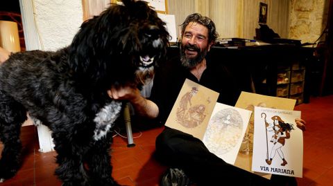Víctor Rivas, con su perro, Gengis Kan, y sus ilustraciones en su estudio y casa de la aldea de Trabazo, en Cotobade.
