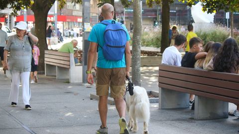 Un chico pasea con su perro atado por la plaza de Pontevedra de A Coruña