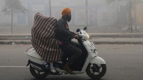 Un hombre traslada a sus hijas hasta el colegio en moto tapadas con una manta para tratar de evitar que les afecte la contaminacin que estos das llena el aure de India.