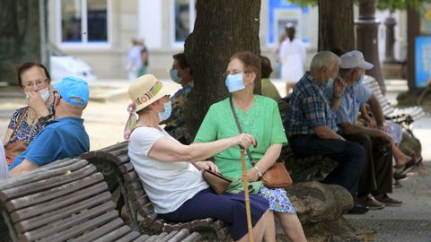 Gente mayor resguardada del sol en los bancos de la Praza Maior