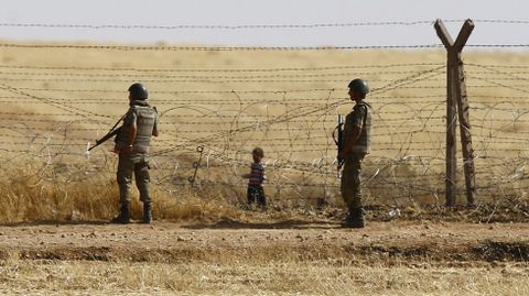 Soldados turcos vigilan la frontera mientras un nio refugiado sirio espera detrs para tratar de cruzar a Turqua