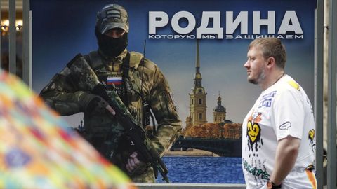 A man walks past a poster depicting a Russian soldier in St. Petersburg