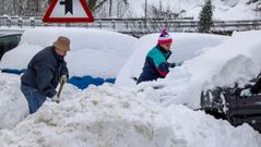 unos vecinos tratan de quitar la nieve de sus vehiculos en el pueblo de Pajares