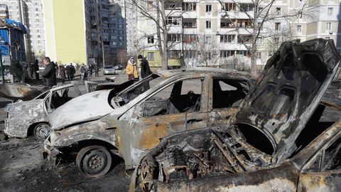 Un da despus de un bombardeo en una zona residencial de Kiev, Ucrania, varias personas pasan junto a coches quemados.