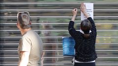 Una mujer coloca un aviso en la persiana cerrada de un negocio del centro de Oviedo